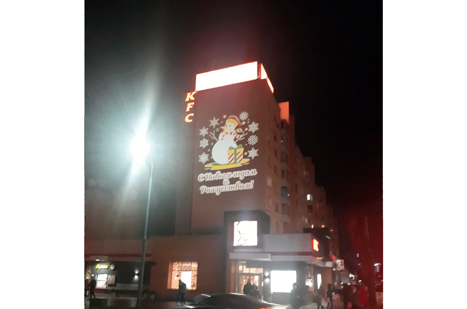 Социальная реклама на фасаде здания. <br>Поздравление с Новым годом и Рождеством. ГОБО-проектор GOSLAID 40008, вращающийся, мощностью 400Вт, рассчитан на 9 рекламных слайдов. Трехцветная проекция.